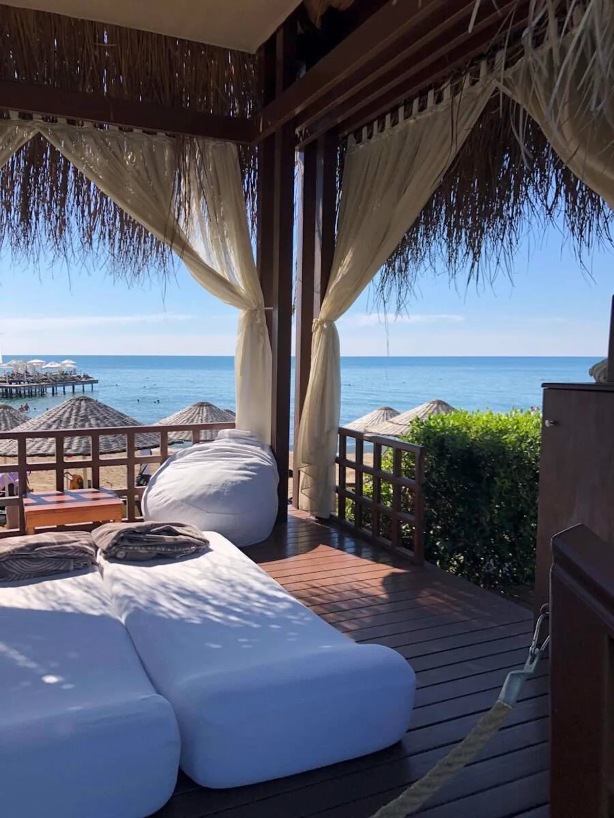 Massagecabana met ligbedden en witte gordijnen op een houten vlonder boven de zee